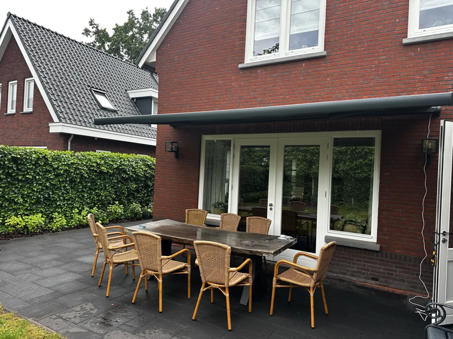 Antraciet zonnescherm uitgeschoven over een terras met tuinset